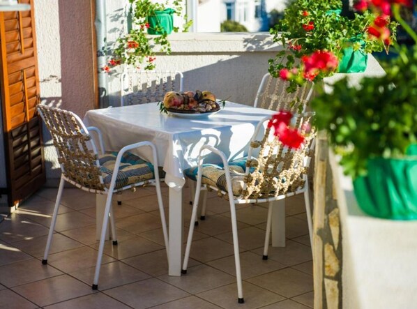 Eine Terrasse im Freien mit Tisch und Stühlen, einem Blumentopf und einem Fenster mit Aussicht.