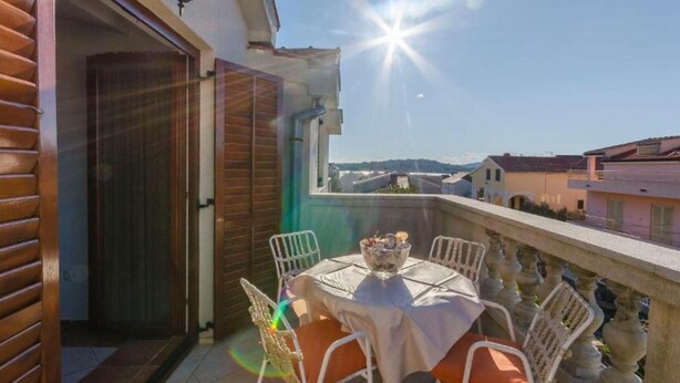 Ein Balkon mit Tisch und Stühlen, Blick auf die Stadt und klarer Himmel.