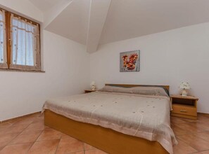 A bedroom with a bed, a nightstand, a lamp, a window with curtains, and a painting on the wall. - Classic One Bedroom Apartment with Terrace (Vodice)
