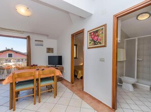 Una habitación con una mesa de comedor, sillas, un televisor, un cuadro y un baño con inodoro y ducha.