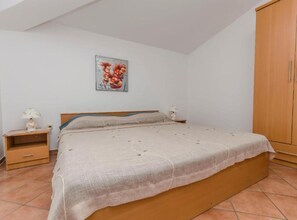 Un dormitorio con una cama, dos mesitas de noche, un armario de madera y un cuadro floral en la pared.