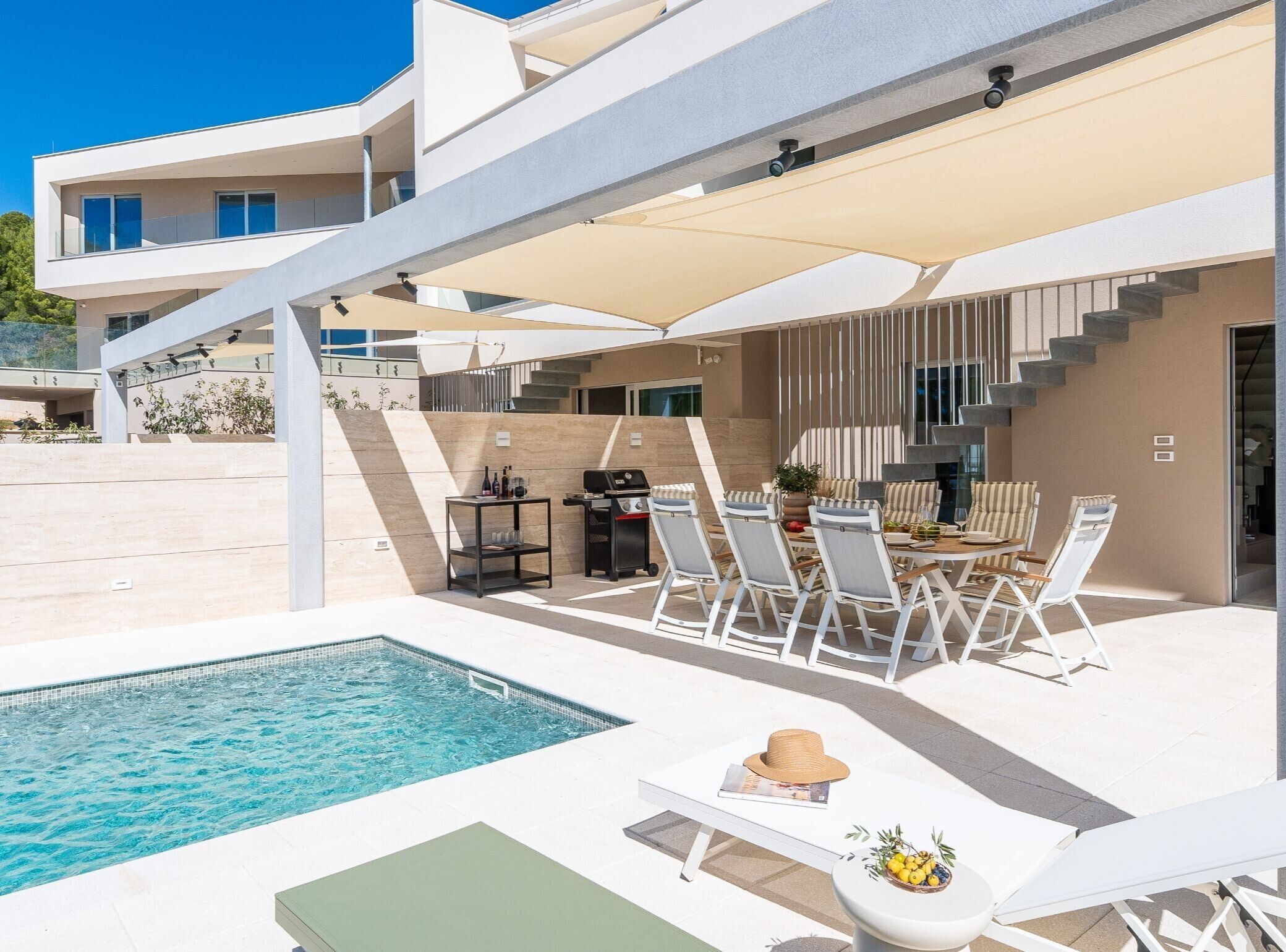 Un área de piscina moderna al aire libre con mobiliario para comer y sillones de descanso.