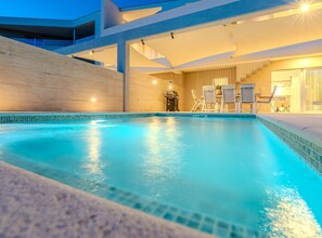 Ein moderner, überdachter Pool mit klarem, blauem Wasser, einer Sitzgruppe im Wasser und Blick zum Himmel.