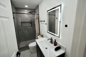 A modern bathroom with a glass-enclosed shower, a white sink with a mirror, and a toilet. - 6370 Atlanta House (Hollywood)