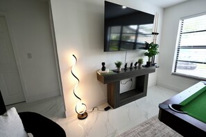 Un salon moderne avec un téléviseur à écran plat fixé au mur, une cheminée agrémentée d’objets décoratifs, une table de billard et une lampe.