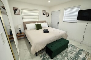Un dormitorio con cama, mesitas de noche, un banco, televisor y una puerta.