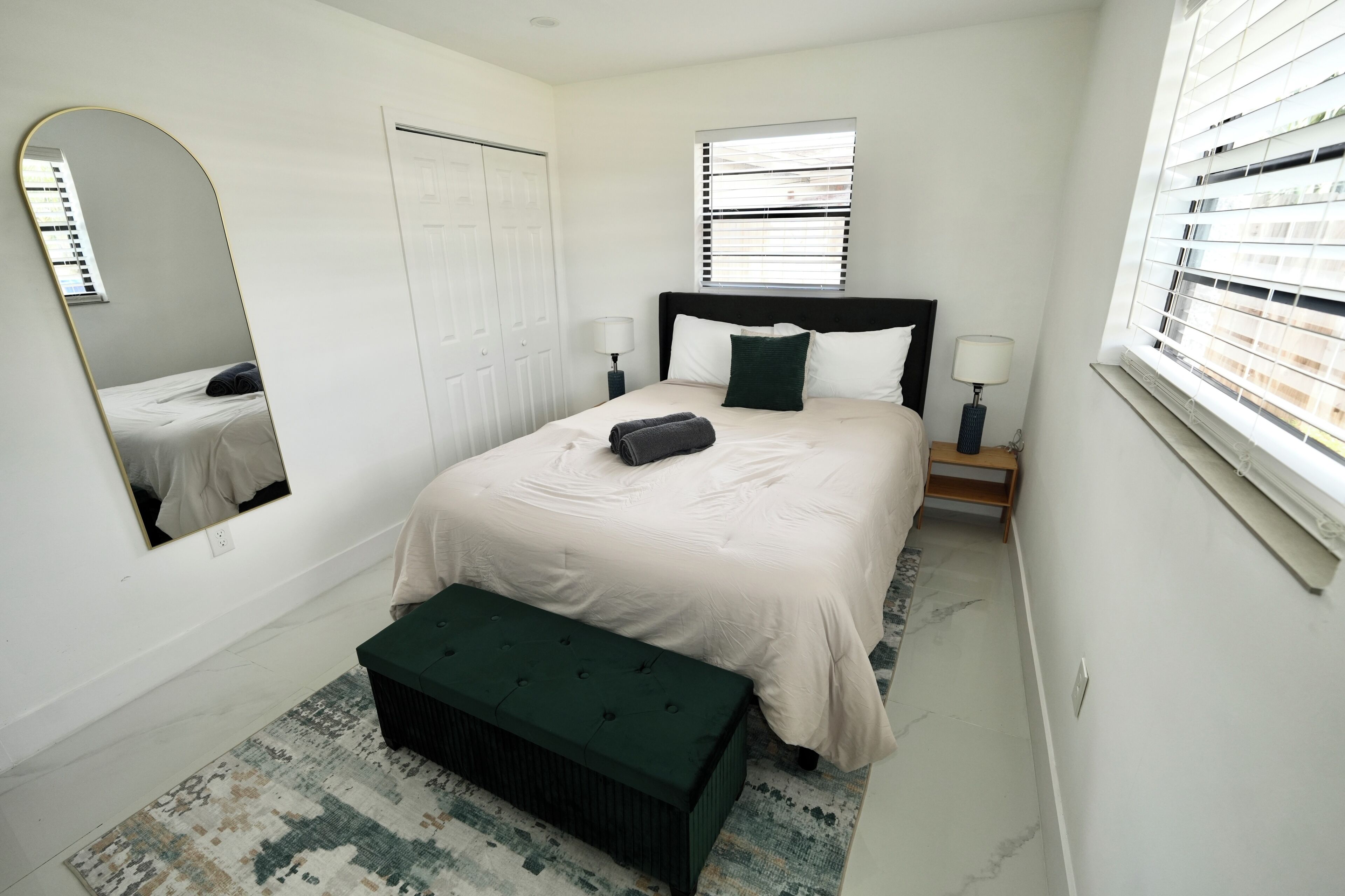 Un dormitorio con cama, un banco, un espejo, una ventana y una puerta.