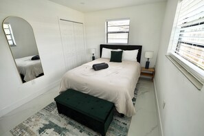 A bedroom with a bed, a bench, a mirror, a window, and a door. - 6370 Atlanta House (Hollywood)