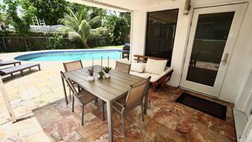 A patio with a pool, outdoor furniture, and a door leading to a covered area.