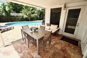 Een terras met een zwembad, tuinmeubilair en een deur naar een overdekt gedeelte.