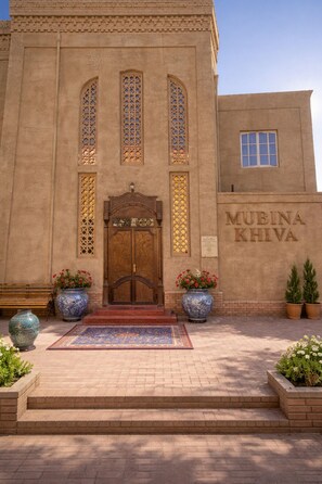 Un edificio con una amplia puerta de madera, un letrero que dice 'MUBINA KHIVA' y una zona de entrada con azulejos.