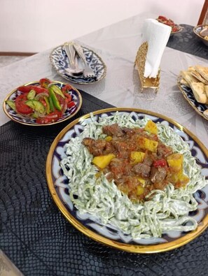 A dining table with a plate of food, a bowl of salad, and a basket of bread.
