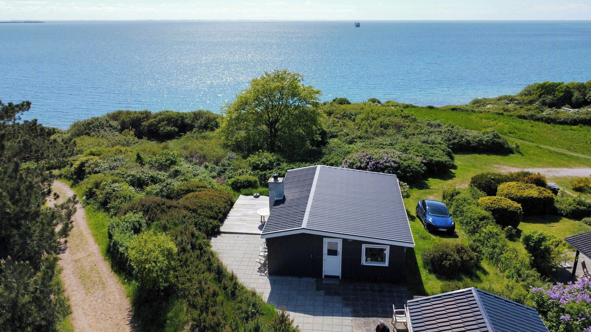 Una casa con techo inclinado, camino de entrada pavimentado y vista al mar.