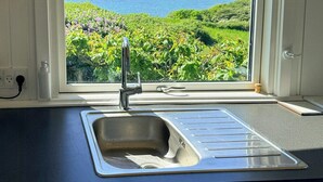 Una cucina con vista sulla costa, un lavello in acciaio inossidabile e un piano di lavoro bianco.