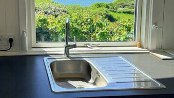 Una cocina con vista al paisaje costero, un lavamanos de acero inoxidable y una encimera blanca.