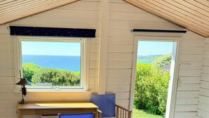 Una camera da letto con un letto, una scrivania, due sedie, una finestra vista mare e una porta che dà sull'esterno.