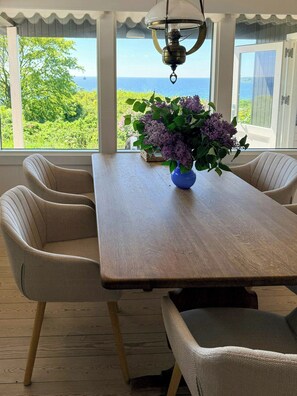 A dining area with a table, chairs, a vase with flowers, and a view of the sea.