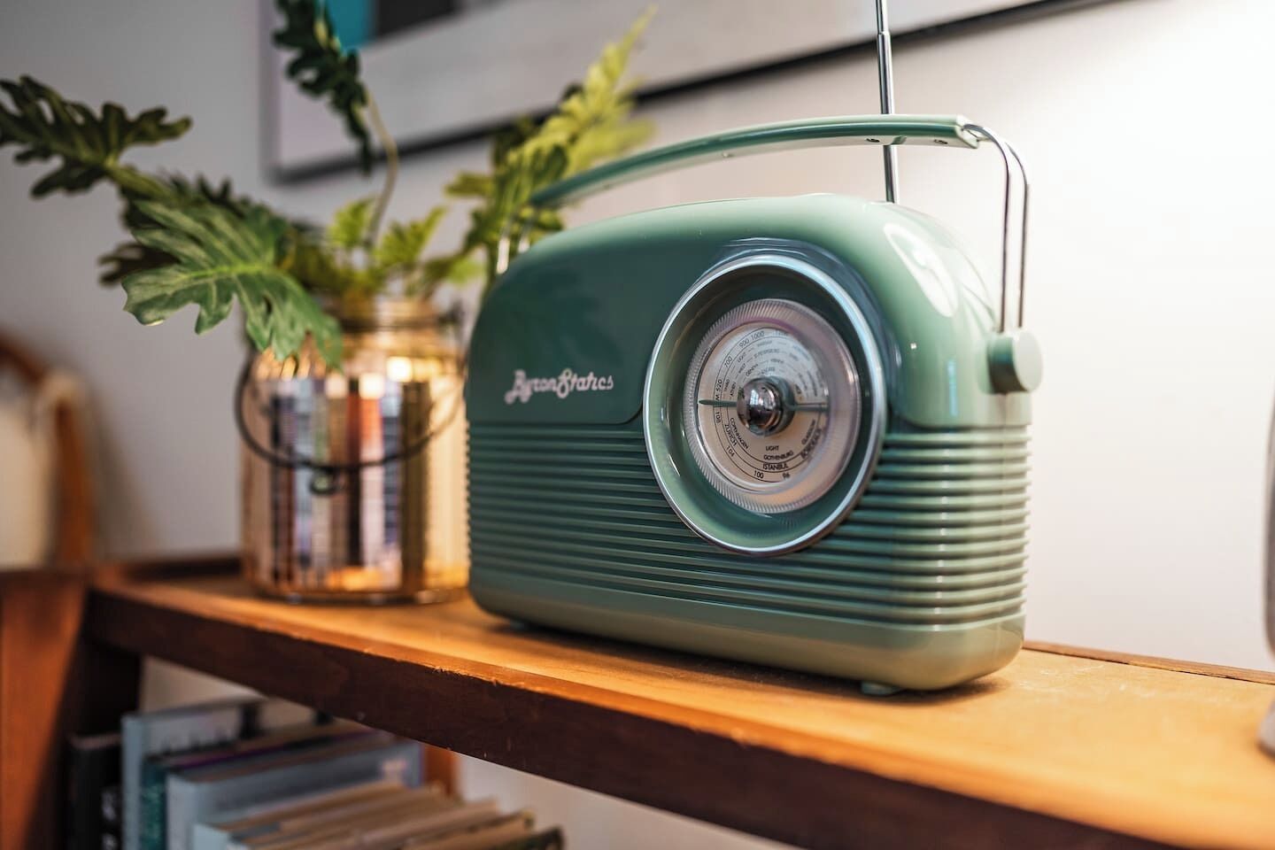 Una radio antigua sobre una repisa de madera, con una planta y libros al fondo.