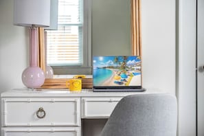 A laptop on a white dresser with drawers, a pink lamp, and a yellow mug with a smiley face. - Cheeky Tiki | Walk to Sound Beach, Fire Pit, Hammock & Fenced Yard (Morehead City)