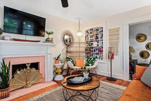 A living room with a fireplace, a television, a bookshelf, and a decorative chair. - Cheeky Tiki | Walk to Sound Beach, Fire Pit, Hammock & Fenced Yard (Morehead City)