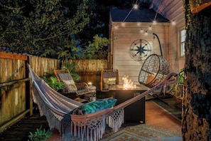 A hammock, two wicker chairs, a fire pit, and a compass wall decoration in a cozy outdoor setting. - Cheeky Tiki | Walk to Sound Beach, Fire Pit, Hammock & Fenced Yard (Morehead City)