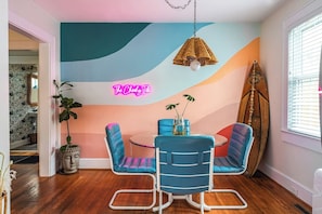 Une pièce avec un panneau lumineux au néon, une planche de surf et une table ronde entourée de chaises.