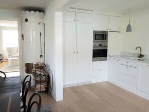 Una cocina con armarios blancos, horno empotrado, microondas y una lámpara colgante.