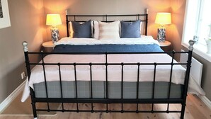 Ein Bett mit schwarzem Metallgestell, zwei Nachttischlampen und ein Fenster zur Rechten.