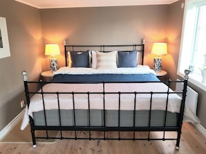 Una cama con estructura de metal negro, dos lámparas de noche y una ventana a la derecha.