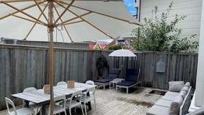 Eine Holzterrasse mit Tisch, Stühlen, einem großen Sonnenschirm und einer Sitzecke.