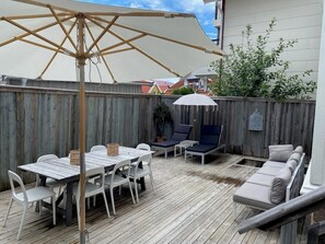 Una terraza de madera con una mesa, sillas y un sofá, además de un paraguas grande.
