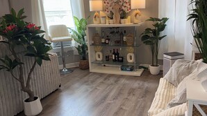 A modern living room with a wooden floor, a white armchair, a glass coffee table, and a decorative shelf with plants and bottles. -  The Langley Luxe Modern style unit (Chicago)