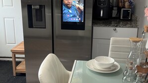 A stainless steel refrigerator with a built-in screen, a dining table with white plates, and a chair. -  The Langley Luxe Modern style unit (Chicago)