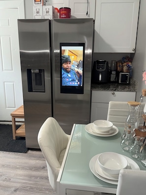 A stainless steel refrigerator with a built-in screen, a dining table with white plates, and a chair. -  The Langley Luxe Modern style unit (Chicago)