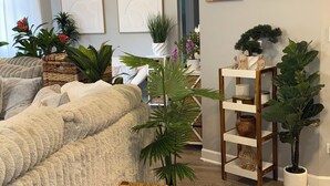 A living room with a sofa, a ceiling fan, a wooden bench, and various plants. -  The Langley Luxe Modern style unit (Chicago)