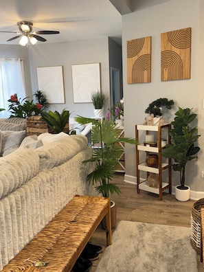 A living room with a sofa, a ceiling fan, a wooden bench, and various plants. -  The Langley Luxe Modern style unit (Chicago)