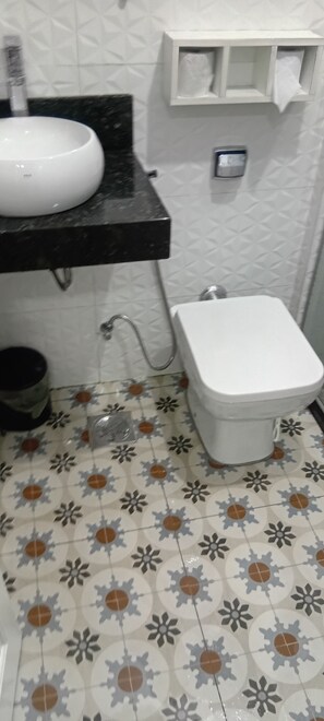 Et badeværelse med toilet i hvid farve, håndvask med sort bordplade og gulvfliser med mønster.