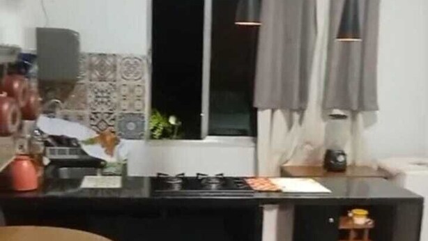 Une cuisine compacte avec un îlot central, un coin repas avec une chaise et une fenêtre avec des rideaux.