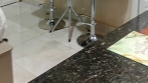 Une cuisine dotée d’un comptoir en granit, de deux tabourets de bar, d’une petite table ronde et d’un téléviseur fixé au mur.