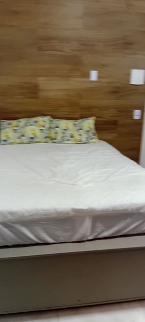 Ein Bett mit Holz-Kopfteil, einem blumigen Kissen und einer weißen Matratze.