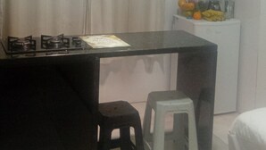 Une cuisine équipée d’une cuisinière à gaz, d’un plan de travail noir, d’un réfrigérateur blanc et d’un petit tabouret.
