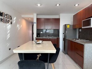 A modern kitchen with dark wooden cabinets, a stainless steel refrigerator, a microwave, and a granite countertop. - Marina del Sol con Vista al Mar | by GPS (Mazatlán)