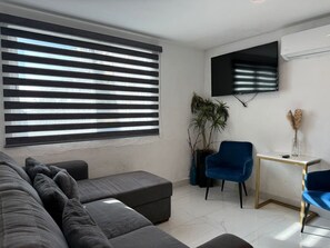 A modern living room with a sofa, ottoman, blue chairs, a TV, and a potted plant. - Marina del Sol con Vista al Mar | by GPS (Mazatlán)