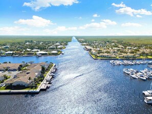 A marina with boats docked, a long pier extending into the water, and residential buildings along the shore.