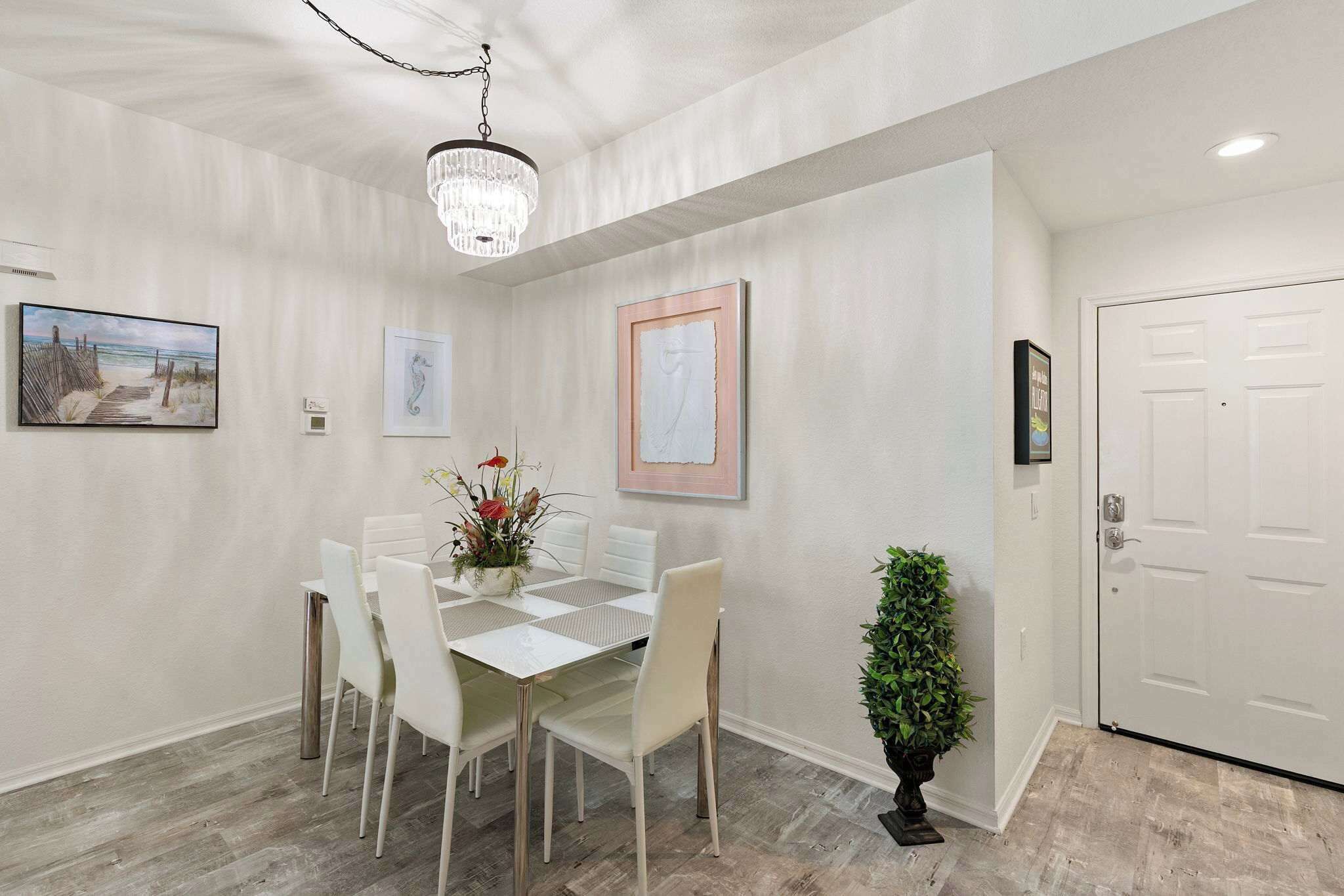 A dining area with a white table and chairs, a chandelier, and framed artwork on the walls.