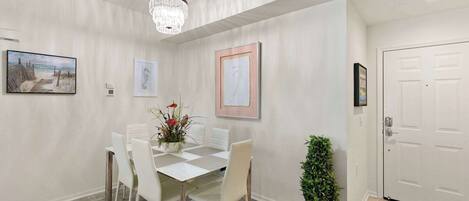 A dining area with a white table and chairs, a chandelier, and framed artwork on the walls.