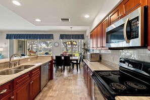 A kitchen with wooden cabinets, a stainless steel refrigerator, a microwave, a stove, and a dining area with a table and chairs.