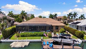 A waterfront property with a covered pool, docked boats, and a large house with a tiled roof. - Marco Island Bayfront Pool & Spa (Marco Island)