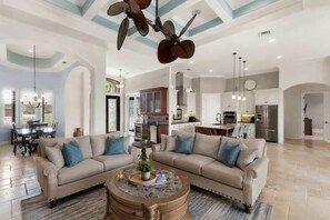 Ein geräumiges Wohnzimmer mit Ecksofa, Couchtisch und Deckenventilator.