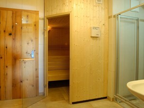 Et træinteriør med sauna, glasbrusekabine og synligt kontrolpanel til saunaen.